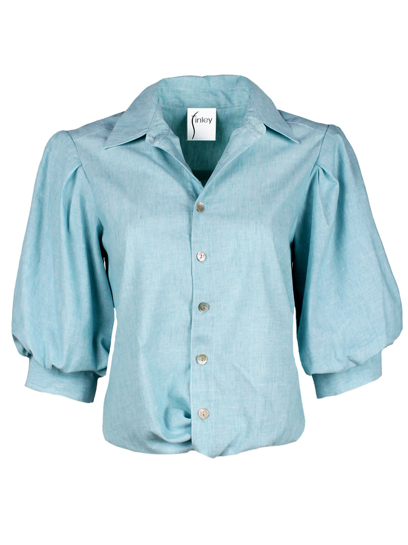 A front view of the Finley Bomba blouse, a light teal button-down shirt with elbow blouson sleeves and a front twist hem detail.