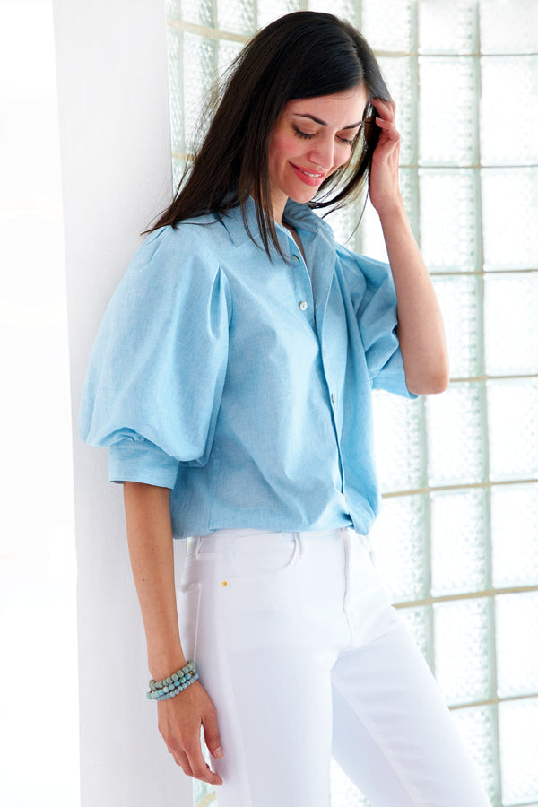A model wearing the Finley Bomba blouse, a light purple  button-down shirt with elbow blouson sleeves and a front twist hem detail.