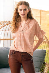 A model wears Finley Crosby, a short sleeve womens blouse with ruffle collar and sleeve details and a geometric orange pattern.