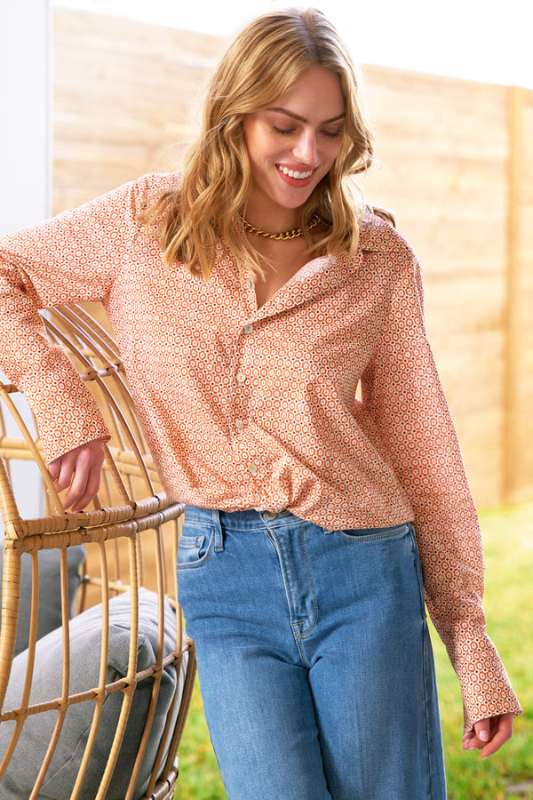 A model wears Finley Moxie, a cotton sateen blouse with a cropped relaxed shape, a twist hem, and an orange geometric print.