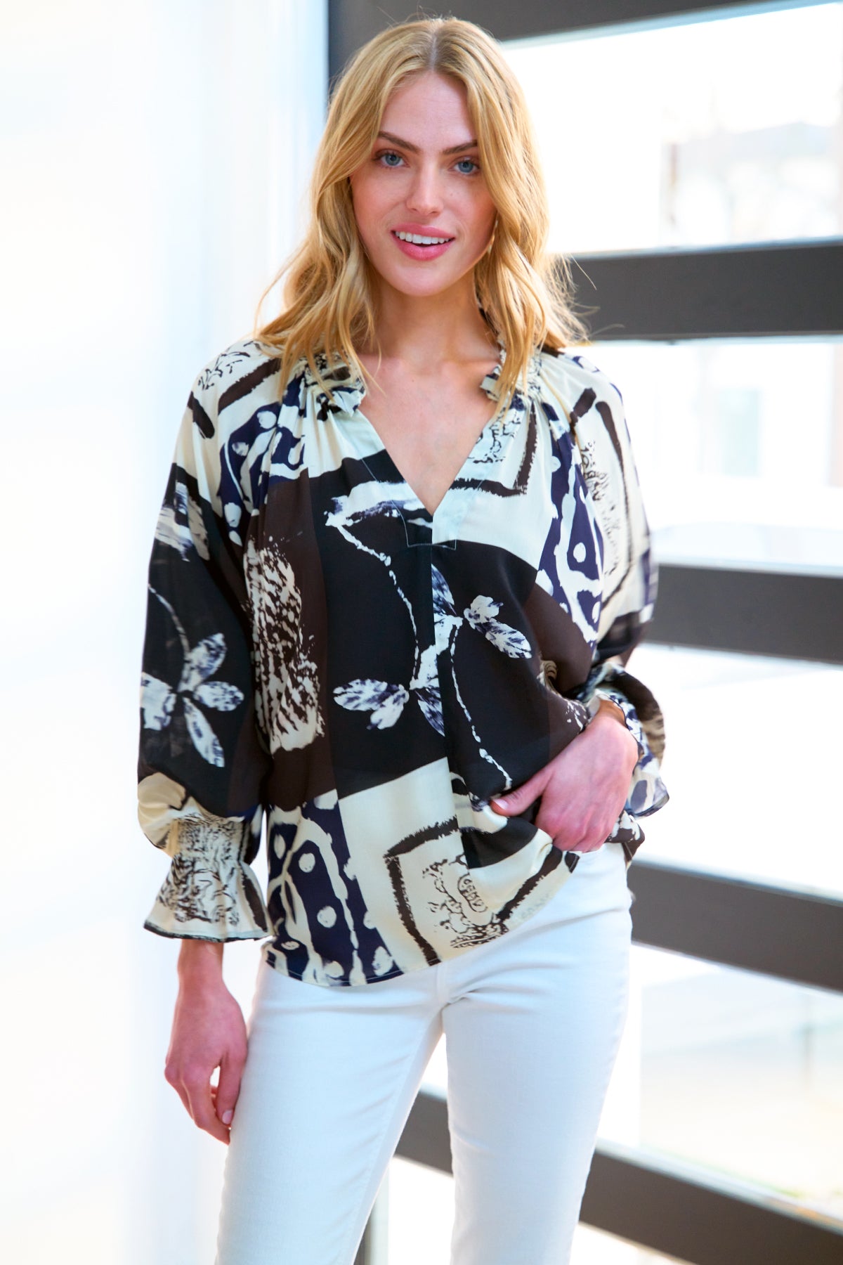 A model wearing the Candace blouse, featuring ruffle trim, a popover design, oversize fit, blouson sleeves, and a black & white Asian abstract print in rayon.
