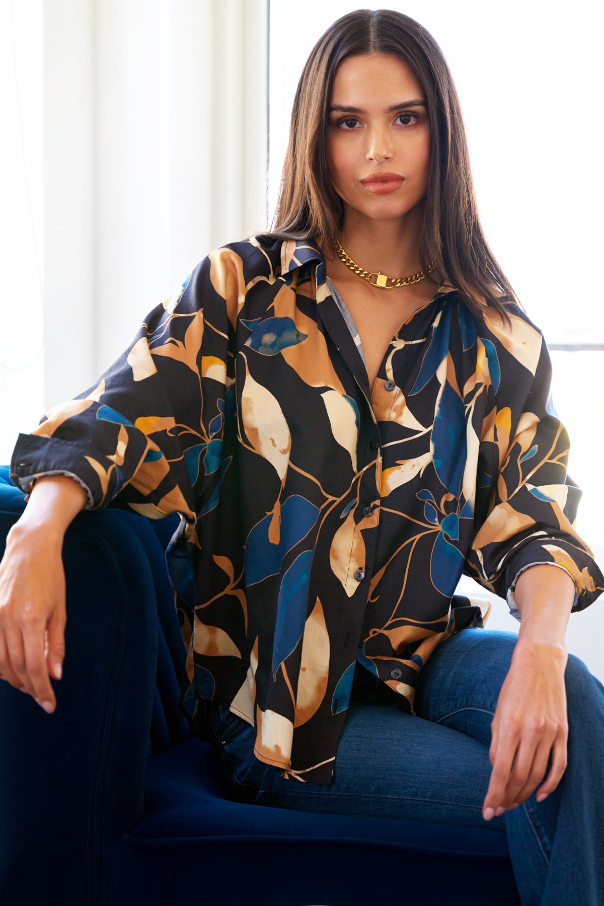 A model wearing the Dylan shirt, featuring dolman sleeves, a shirttail hem, ruched neckline, oversize contour, 100% cotton, and navy and bronze floral print.
