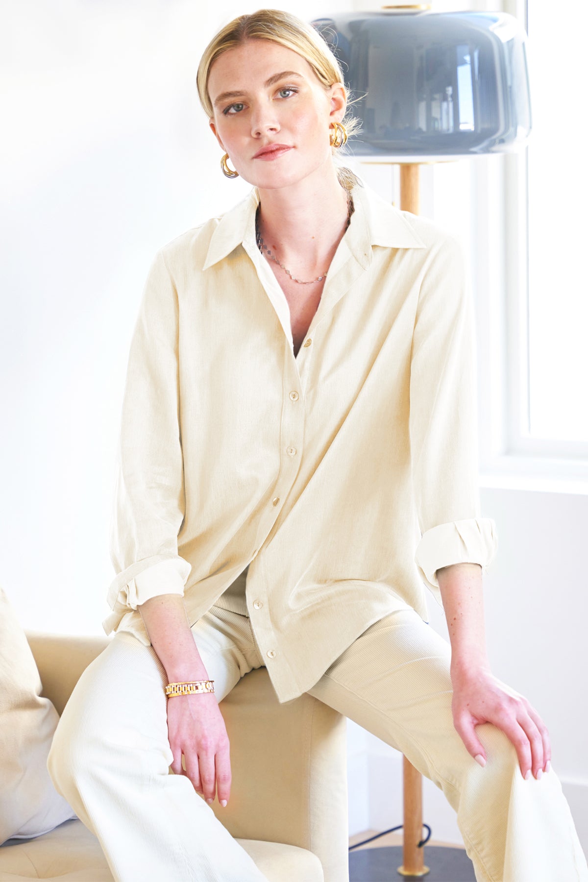 A model wearing the Mini Monica shirt, crafted from cupro and cotton in cream, featuring a spread collar, relaxed fit, shirttail hem, and long sleeves.
