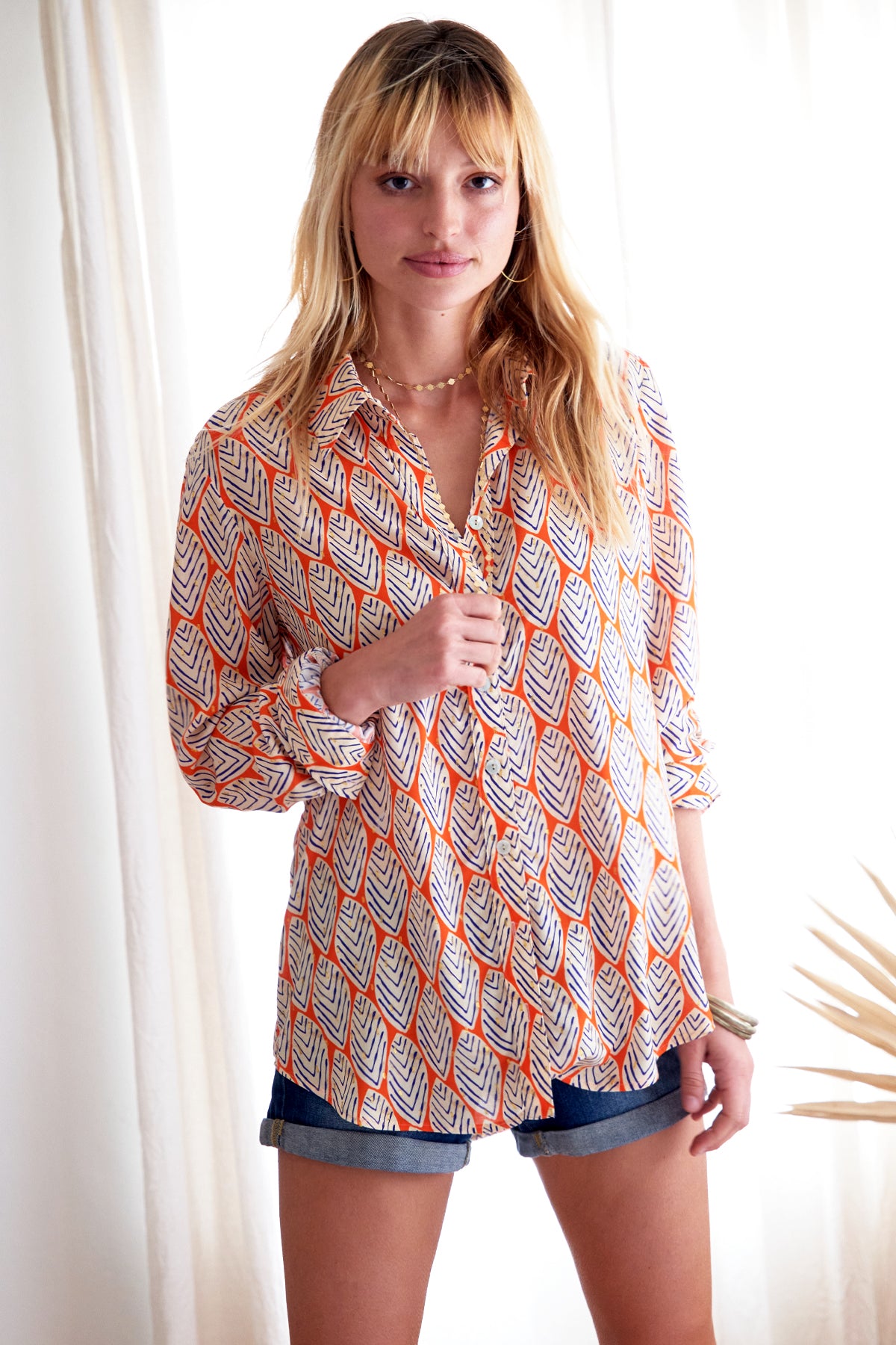 The Finley Mini-Monica blouse, a v-neck button-down blouse with a spread collar and a orange and white leaf pattern.