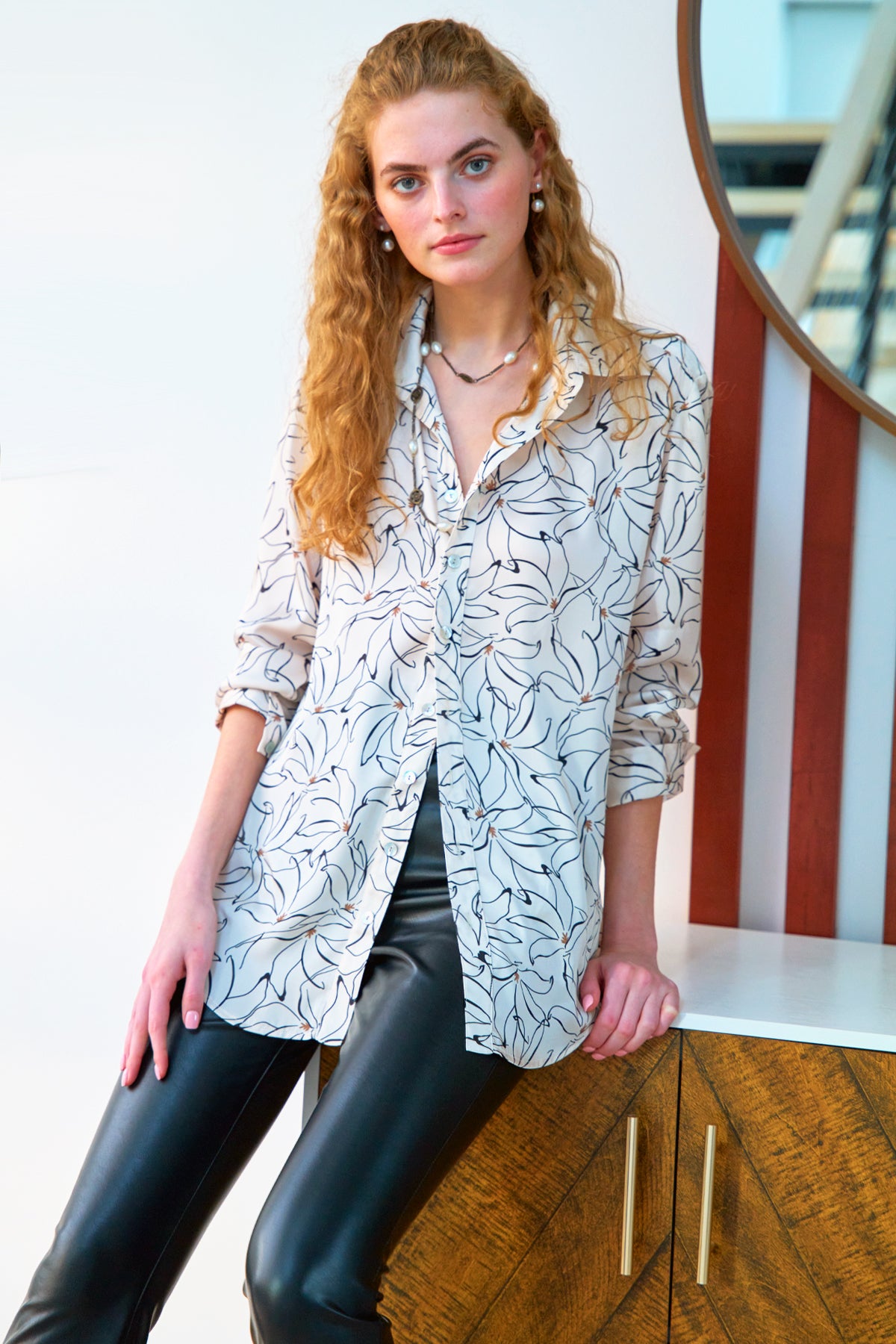 A model wearing the Monica oversize blouse, featuring a black and gold floral pattern, spread collar, oversize fit, and made from polyester.