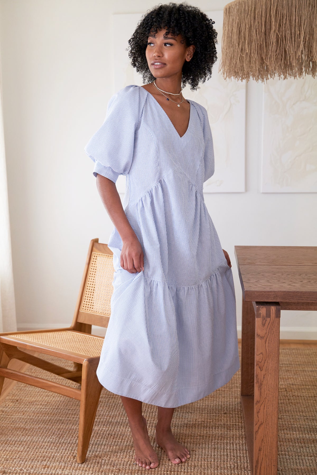 A Black supermodel wearing Finley Paloma dress, a blue seersucker stripe v-neck maxi dress with puff short sleeves and ruffle hem.